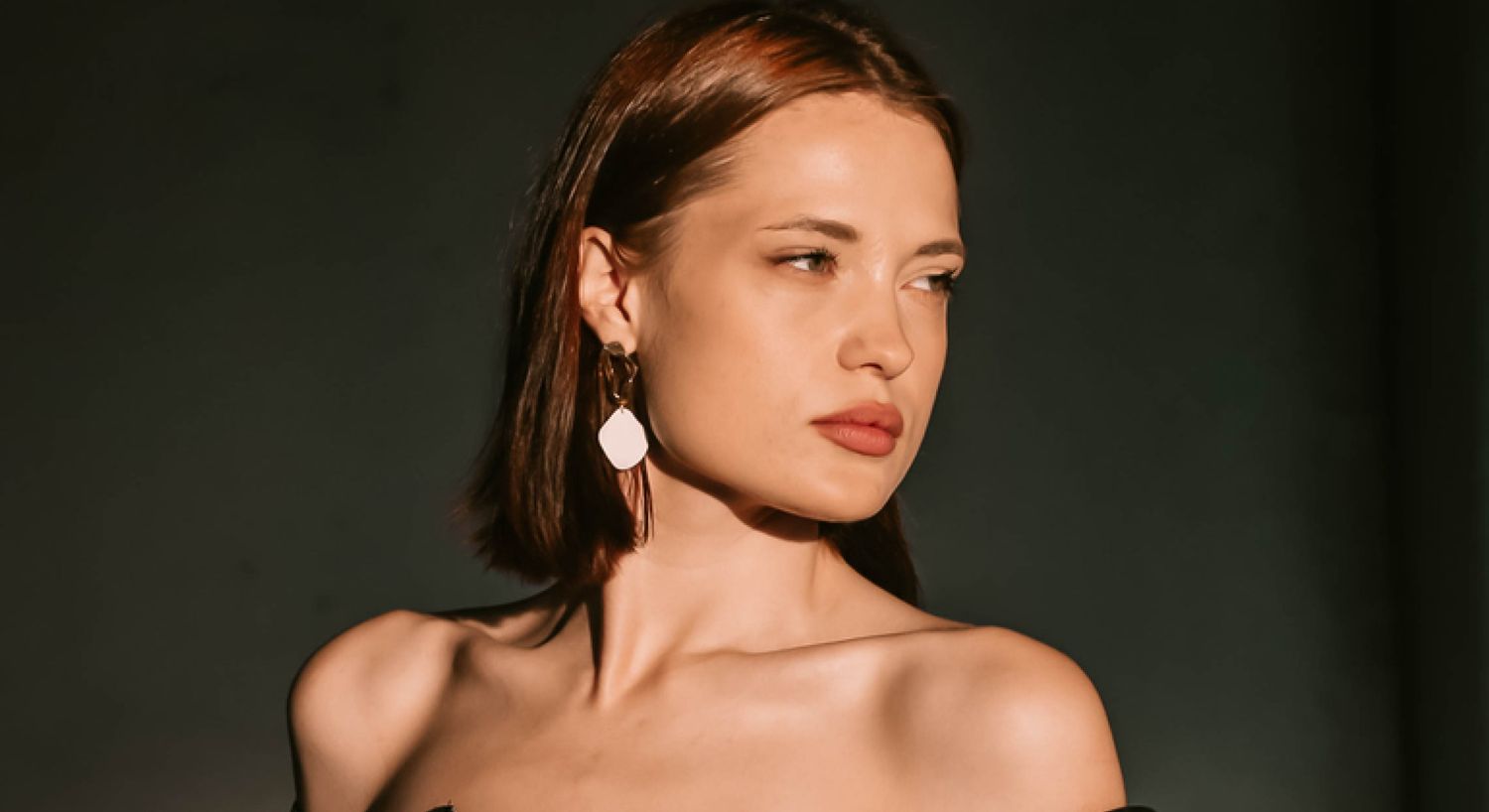 Model with elegant earrings against a dark background.