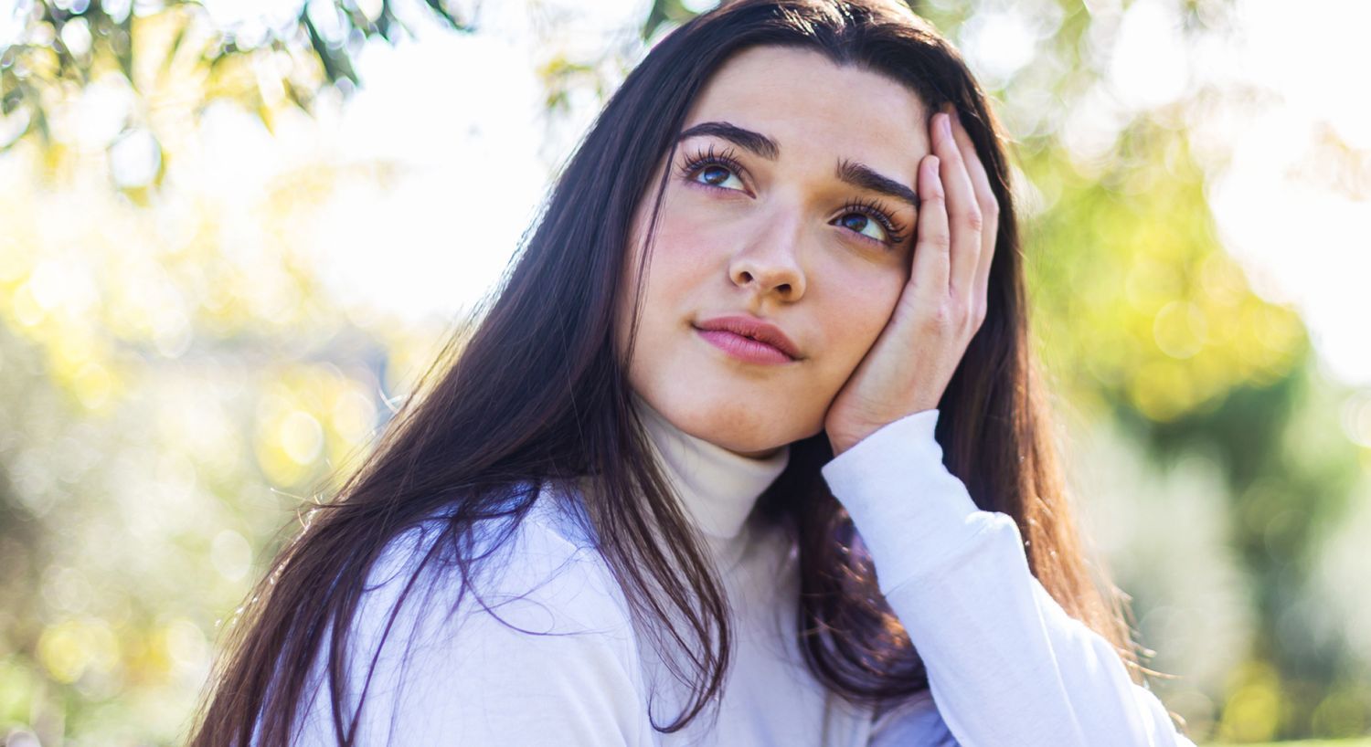 Woman contemplating outdoors with a thoughtful expression.